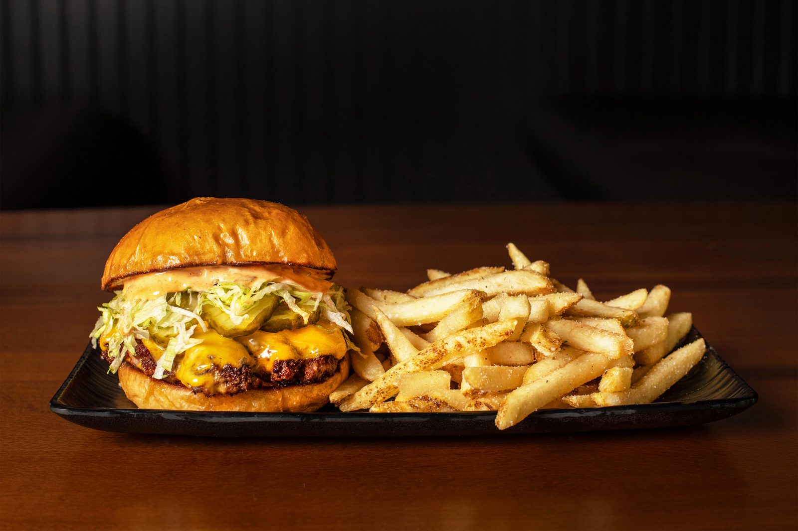 A Ground Rules smashburger and seasoned fries plated on a board.