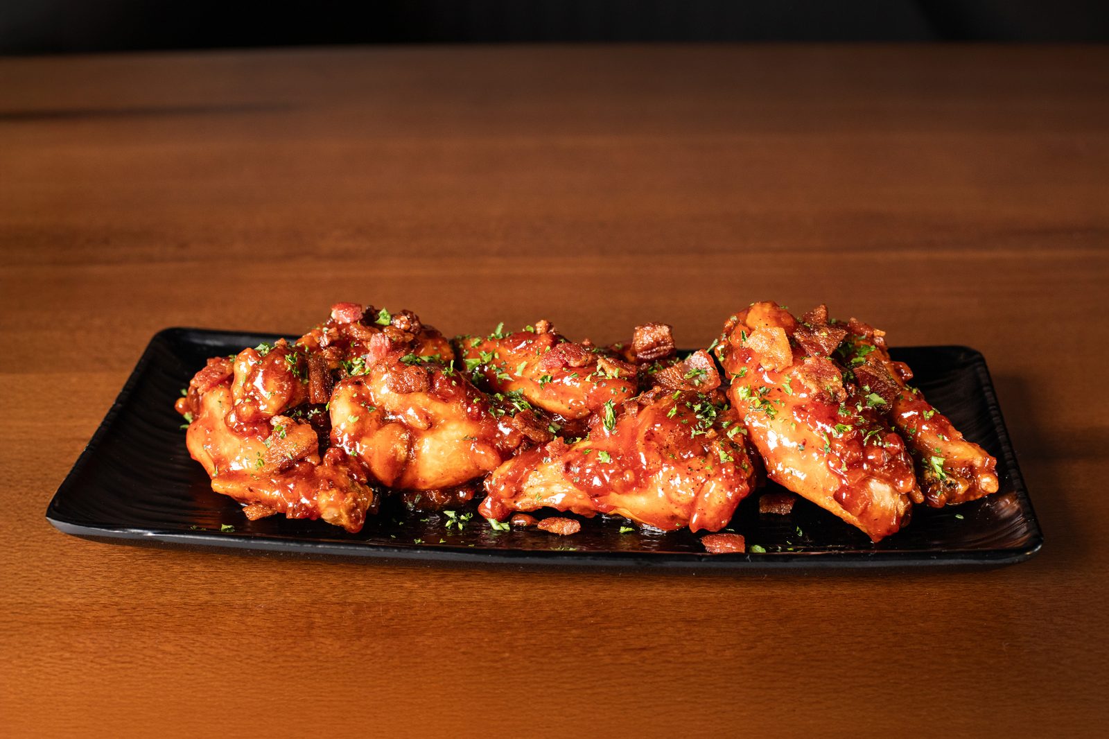 Twice-fried wings glazed and lined up on a long board.